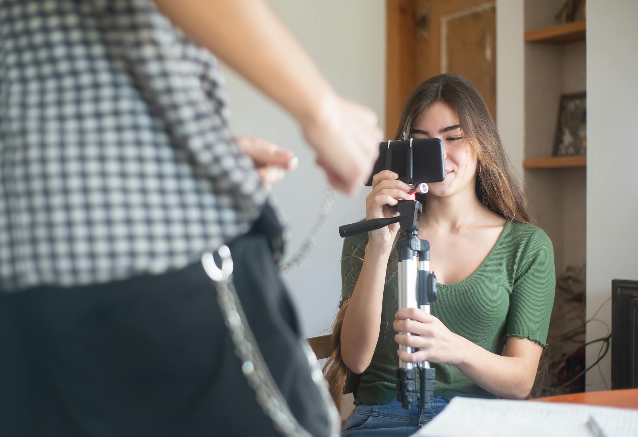 A young woman vlogs indoors using a smartphone mounted on a tripod, capturing content creation.